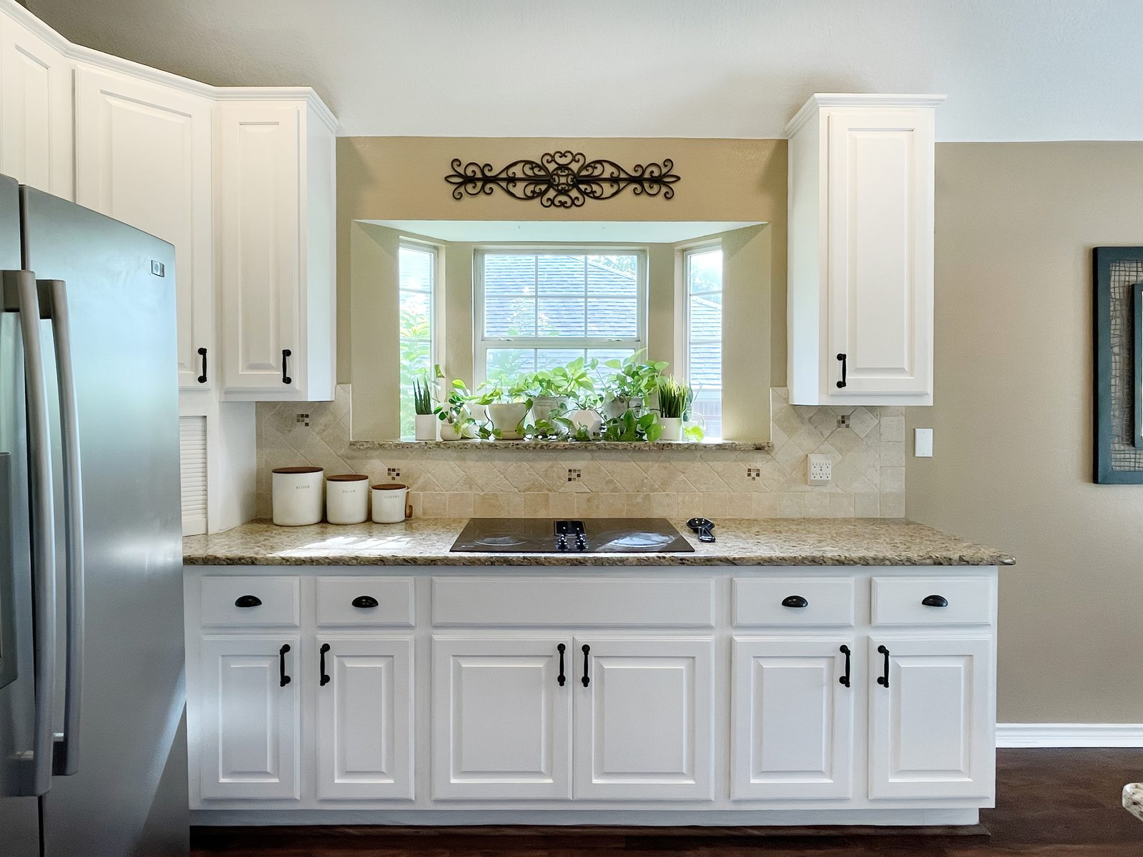 The same cooktop wall after, white cabinets and plants in the bay window